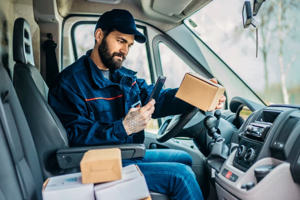 A delivery courier uses a phone to scan a parcel before leaving it with a customer.