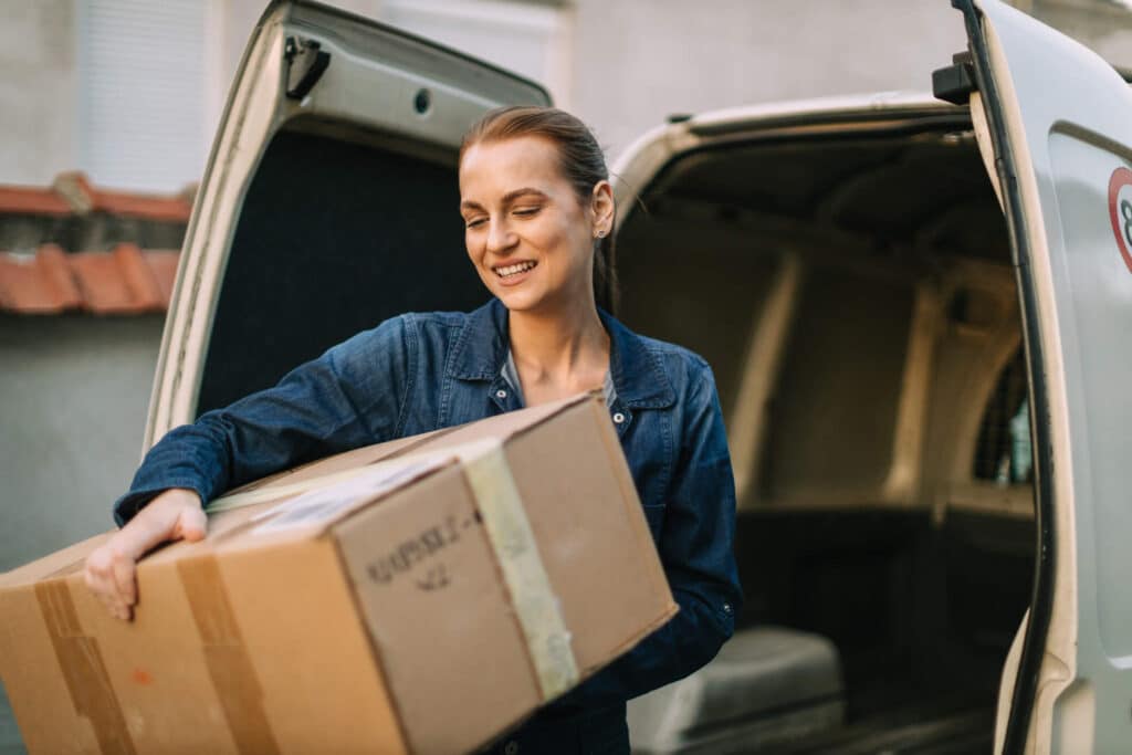 Young woman works as a courier delivering packages in a white van on a sunny day on the city street.