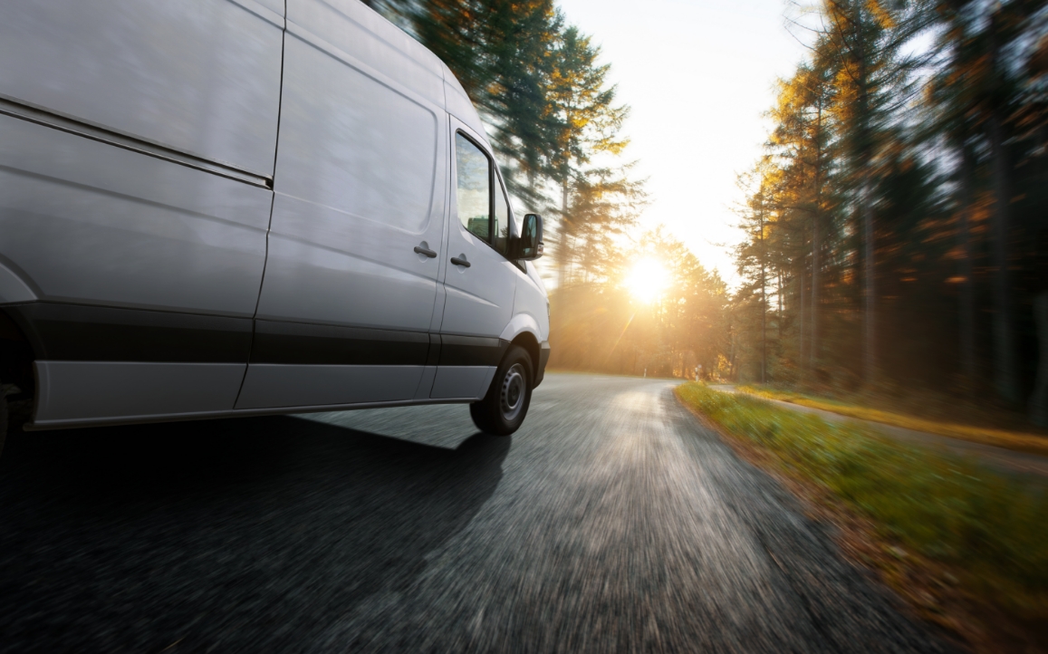 A van driving through a paved road in a forest